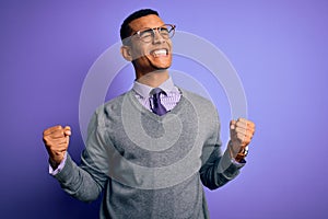 Handsome african american businessman wearing glasses and tie over purple background very happy and excited doing winner gesture