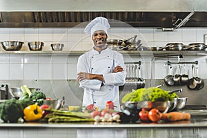 handsome african american chef standing at restaurant kitchen with crossed arms and looking