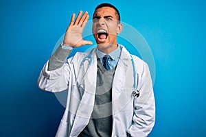 Handsome african american doctor man wearing coat and stethoscope over blue background shouting and screaming loud to side with