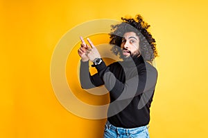 Handsome african american guy in surprise shows his forefingers to the top and looks at the camera