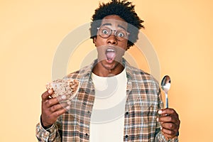 Handsome african american man with afro hair eating healthy whole grain celears with spoon celebrating crazy and amazed for