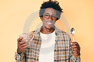 Handsome african american man with afro hair eating healthy whole grain celears with spoon smiling with a happy and cool smile on