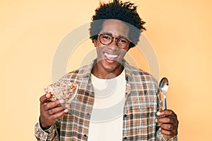 Handsome african american man with afro hair eating healthy whole grain celears with spoon smiling and laughing hard out loud