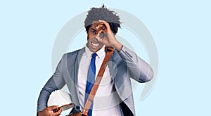 Handsome african american man with afro hair holding architect hardhat smiling happy doing ok sign with hand on eye looking