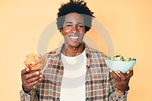 Handsome african american man with afro hair holding nachos and healthy salad smiling with a happy and cool smile on face