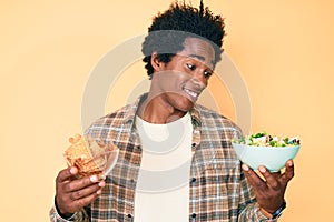 Handsome african american man with afro hair holding nachos and healthy salad smiling looking to the side and staring away