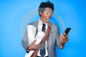 Handsome african american man with afro hair holding paper blueprints using smartphone celebrating crazy and amazed for success