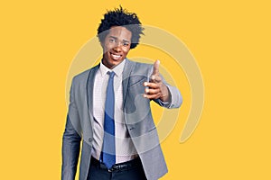 Handsome african american man with afro hair wearing business jacket smiling friendly offering handshake as greeting and welcoming