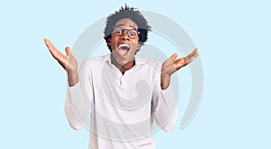 Handsome african american man with afro hair wearing casual clothes and glasses celebrating crazy and amazed for success with arms