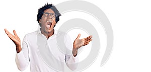 Handsome african american man with afro hair wearing casual clothes and glasses celebrating mad and crazy for success with arms