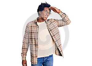 Handsome african american man with afro hair wearing casual clothes and glasses very happy and smiling looking far away with hand