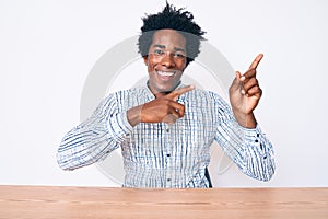 Handsome african american man with afro hair wearing casual clothes sitting on the table smiling and looking at the camera