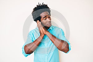 Handsome african american man with afro hair wearing casual clothes sleeping tired dreaming and posing with hands together while