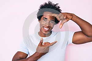 Handsome african american man with afro hair wearing casual clothes smiling making frame with hands and fingers with happy face