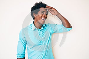 Handsome african american man with afro hair wearing casual clothes very happy and smiling looking far away with hand over head