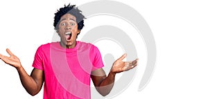 Handsome african american man with afro hair wearing casual pink tshirt celebrating victory with happy smile and winner expression
