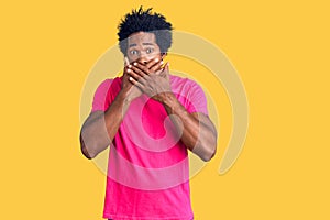 Handsome african american man with afro hair wearing casual pink tshirt shocked covering mouth with hands for mistake