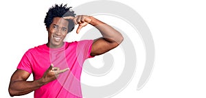 Handsome african american man with afro hair wearing casual pink tshirt smiling making frame with hands and fingers with happy