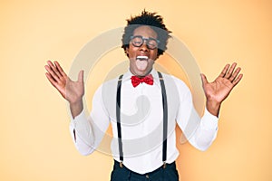 Handsome african american man with afro hair wearing hipster elegant look celebrating mad and crazy for success with arms raised