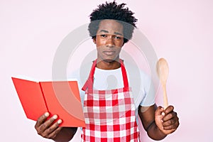 Handsome african american man with afro hair wearing professional baker apron reading cooking recipe book depressed and worry for
