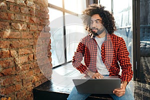 Handsome african american man with black beard works at the computer against the background of a large window