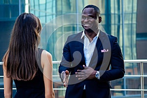 Handsome African American man in a black business suit shaking hand with a businesswoman partner cityscape glass offices