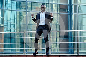 A handsome African American man in a black stylish suit and a white shirt rejoicing in success and thanking God against