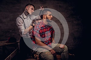 Handsome African American man getting a haircut while sitting on wooden boxes at a studio. Old-fashioned professional