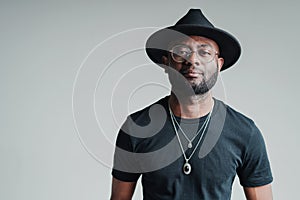 Handsome african american man in glasses wearing hat and black t-shirt  on gray background