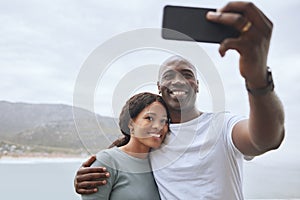Handsome african american man and his beautiful wife taking selfies with a phone against a scenic seascape background. A
