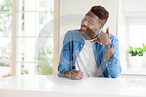 Handsome african american man at home smiling doing phone gesture with hand and fingers like talking on the telephone