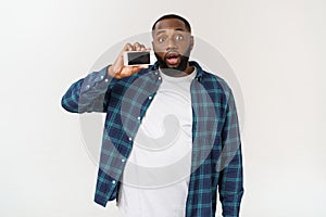 Handsome african american man isolated on grey background, presenting smart phone.