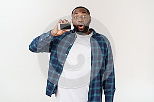 Handsome african american man isolated on grey background, presenting smart phone.