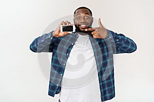Handsome african american man isolated on grey background, presenting smart phone.