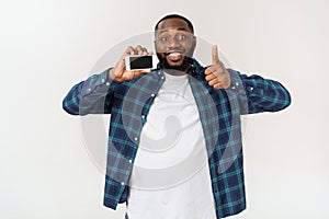 Handsome african american man isolated on grey background, presenting smart phone.