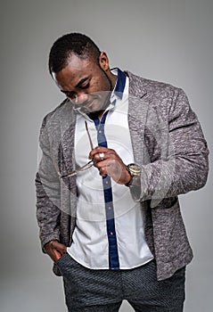 Handsome african american man looking on glasses in hand. Stylish businessman in grey suit and white shirt