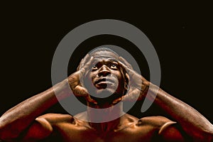 Handsome African american man looking up touching hands of head, portrait of nude dark-skinned athlete isolated on black