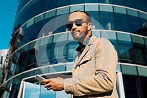 Handsome african american man outdoors speaking on the phone near modern businees centre, side view.