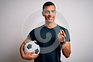 Handsome african american man playing footbal holding soccer ball over white background Beckoning come here gesture with hand