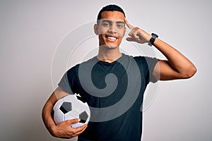 Handsome african american man playing footbal holding soccer ball over white background Smiling pointing to head with one finger,