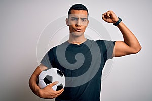 Handsome african american man playing footbal holding soccer ball over white background Strong person showing arm muscle,