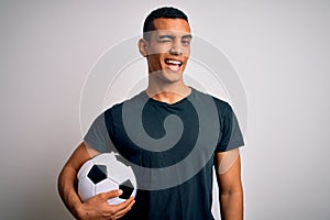Handsome african american man playing footbal holding soccer ball over white background winking looking at the camera with sexy