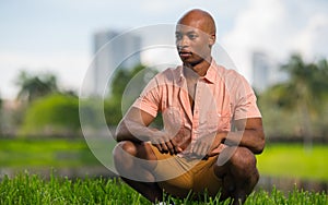 Handsome African American man posing outdoors squatting and glancing away from camera. Pleasing blurry background nature scene