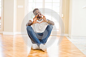 Handsome african american man sitting on the floor at home smiling in love showing heart symbol and shape with hands