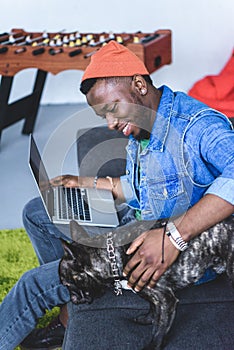 Handsome african american man sitting on sofa with laptop and stroking