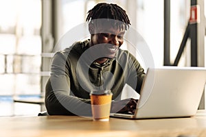 Handsome African American man is typing on a laptop while sitting in a cafe. young student on distance learning at home