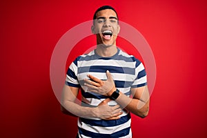 Handsome african american man wearing casual striped t-shirt standing over red background smiling and laughing hard out loud