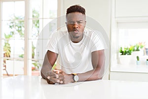 Handsome african american man on white table at home skeptic and nervous, frowning upset because of problem