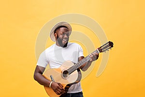 Handsome african american retro styled guitarist playing acoustic guitar isolated on yellow background.