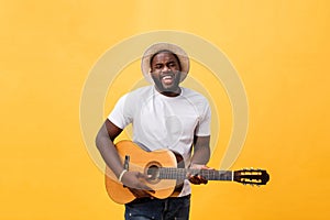 Handsome african american retro styled guitarist playing acoustic guitar isolated on yellow background.